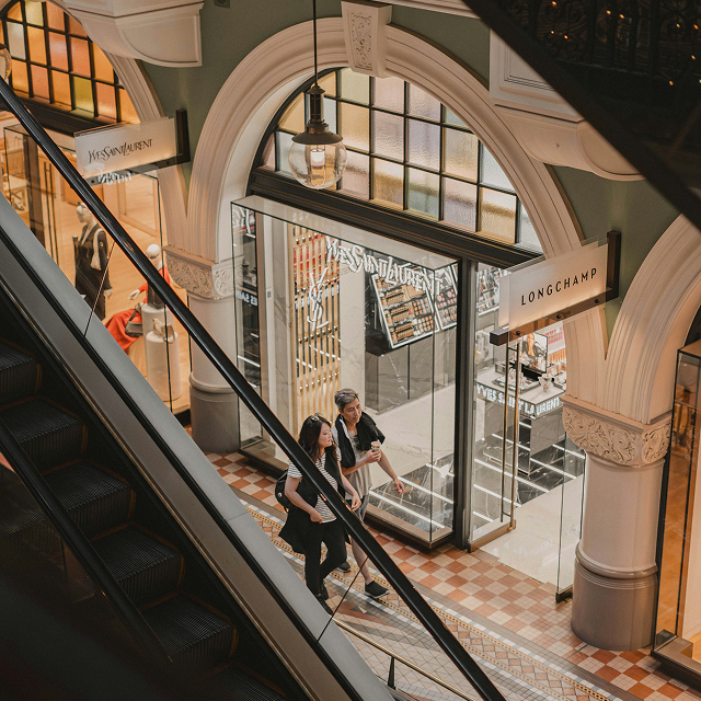 Shoppers on escalator in ornate luxury shopping arcade with designer stores