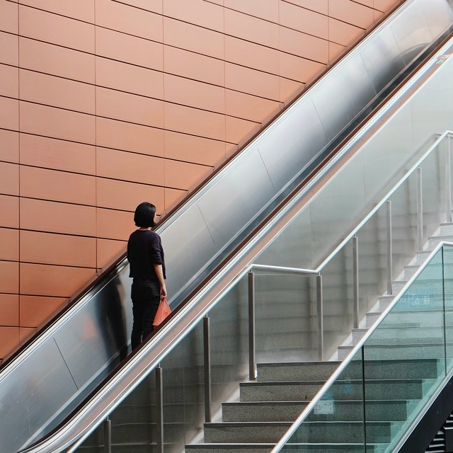 Woman riding an escalator in a transit terminal with copper wall panels