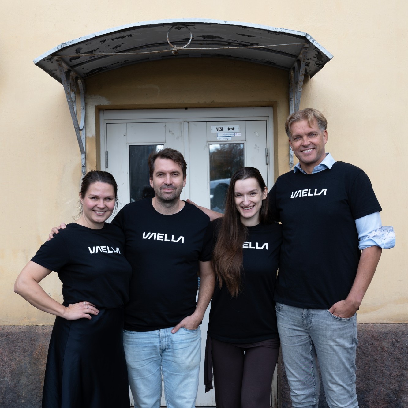 Four members of the VAELLA team in VAELLA T-shirts outside their office entrance